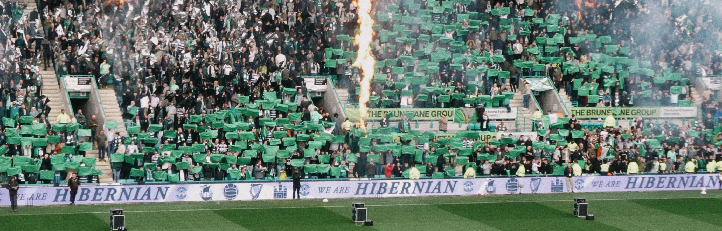 Schottischer Fußball live – Packende Stadionatmosphäre erleben Die Mannschaften laufen im Stadion auf den Rasen ein, während auf der Tribüne im Hintergrund grüner Rauch und Flammensäulen für eine spektakuläre Kulisse sorgen.